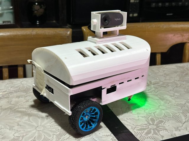 MuseBot AI, fully assembled with its camera mast and LED strip, on a lace tablecloth.